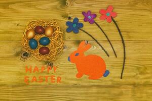 Happy Easter message with painted eggs in straw,bunny and flowers on wooden table.Toned photo. photo