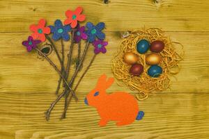 Painted Easter eggs in straw with flowers and bunny on wooden table.Toned photo. photo