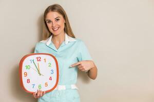 Portrait of medical nurse pointing at clock. photo