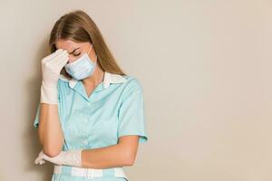 Tired nurse  with protective mask and gloves having headache. photo