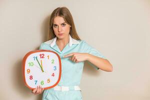 Portrait of angry medical nurse pointing at clock. photo