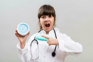 Little doctor is showing that is time to think about health by pointing at clock. photo