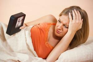 cansado mujer mirando a reloj mientras acostado en su cama foto