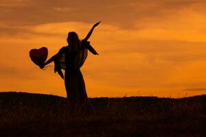 silueta de un mujer participación corazón conformado globo y mirando a hermosa puesta de sol. foto