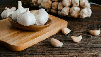 organic Raw garlic bulb, garlic cloves on wooden cup, wooden cutting board, wooden table and garlic cloves of food ingredients photo