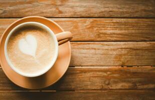 en forma de corazon café latté en un marrón taza con un platillo, metido en un antiguo de madera mesa. ese es Listo a dar usted frescura cada Mañana. foto