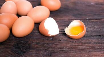 fresh organic chicken eggs and half-broken egg on brown wooden board, photo