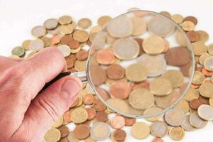 a hand holding a magnifying glass over a pile of coins photo