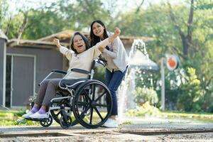 Asian senior woman in wheelchair with happy daughter. Family relationship retired woman sitting on wheelchair in the park age care at retirement home. photo