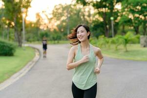 ajuste asiático joven mujer trotar en parque sonriente contento corriendo y disfrutando un sano al aire libre estilo de vida. hembra persona que practica jogging. aptitud corredor niña en público parque. sano estilo de vida y bienestar siendo concepto foto