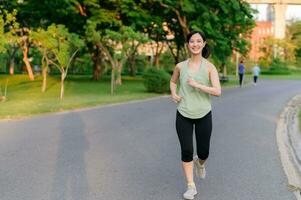 Fit Asian young woman jogging in park smiling happy running and enjoying a healthy outdoor lifestyle. Female jogger. Fitness runner girl in public park. healthy lifestyle and wellness being concept photo