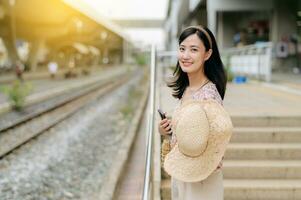 joven asiático mujer viajero con Costura cesta esperando para tren en tren estación. viaje viaje estilo de vida, mundo viaje explorador o Asia verano turismo concepto. foto