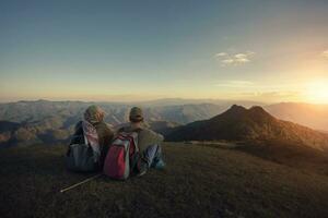 man and woman backpacker sitting on top of high moutain with panorama view of mountain scape photo