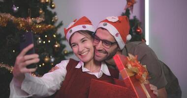 Portrait of Young couple taking selfie and smiling while standing with decorated Christmas tree in the background, celebrating Christmas and New Year, Lovers have moment romantic and happy together. photo