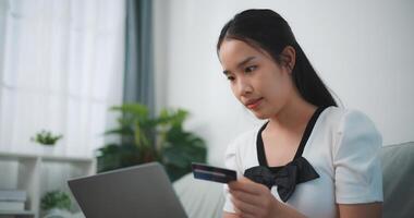 Portrait of Young asian woman sitting on sofa in living room, makes online banking payments through the internet from bank card on laptop,Shopping online with credit card. photo