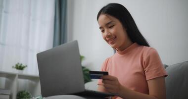 Portrait of Young asian woman sitting on sofa in living room, makes online banking payments through the internet from bank card on laptop,Shopping online with credit card. photo