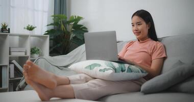 Portrait of Young asian woman relaxing at home sit on comfortable couch using laptop, chatting with friends in social network, do remote job, shopping online photo