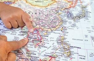 Tourist's hand pointing at world map of Thailand. Located in Southeast Asia, Thailand is a cultural capital of global interest and a destination. top view photo