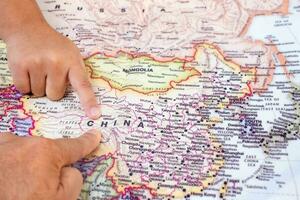 Tourist's hand pointing at world map of China. Located in Asia on world map, China is a country with a large area and a large population. top view photo