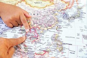 Tourist's hand pointing at world map of Thailand. Located in Southeast Asia, Thailand is a cultural capital of global interest and a destination. top view photo