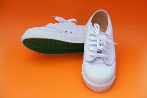 Pair of new white canvas sneakers, one shows green rubber under the shoes , orange background. Comfortable, fashionable. Concept, shoes for doing sport or exercise also can wear for traveling, hiking. photo