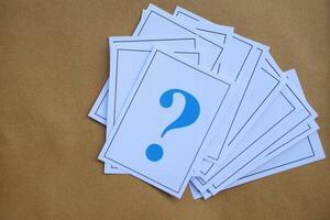 Pile of overlapped paper cards of blue  question marks, brown background. Concept. Teaching aid. Education materials for doing activity or playing games about find answers. photo