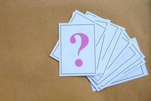 Overlapped pile of paper cards of pink question mark on brown background. Concept. Teaching aid. Education materials for doing activity or playing games about find answers. photo