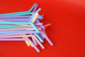 Colorful plastic drinking straws tubes for juice and cocktails, red background. Concept, single use equipment for drinking, but can use for diy crafts for decoration. photo