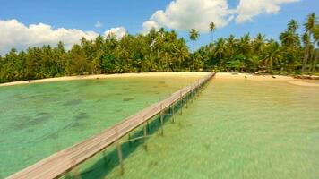 A dynamic drone flight over turquoise ocean, wooden bridge and white sand beach. video