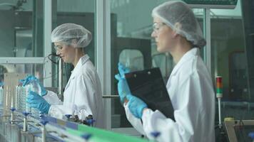 scientist worker checking the quality of water bottles on the machine conveyor line at the industrial factory. Female worker recording data at the beverages manufacturing line production. video