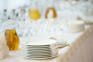 A stack of white plates on the table with a carafe of juice plastic cups photo