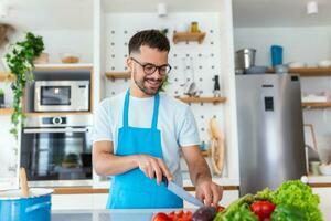 Handsome young man man stand at modern kitchen chop vegetables prepare fresh vegetable salad for dinner or lunch, young male cooking at home make breakfast follow healthy diet, vegetarian concept photo