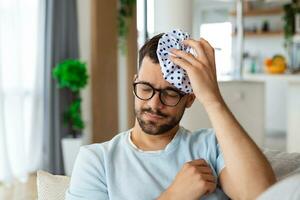 When you hit shelf with your head. Frustrated young man holding ice bag on his head while lying on the couch at home photo