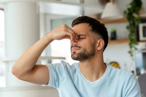 Tired caucasian bearded man sits on the sofa, having a headache. Unhealthy guy catch a cold or having flu, upset about illness, unhappy man feel depressed photo