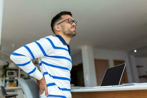 Shot of a young businessman suffering from a backache while working at his desk in his office. photo