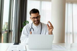 retrato de joven médico hablando a en línea paciente en ordenador portátil pantalla sentado a clínica oficina escritorio dando en línea consulta para Doméstico salud tratamiento. telemedicina remoto médico cita foto