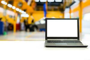 Laptop on white desk with blurred car garage with maintenance and fixing photo