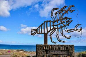 a metal sculpture of a lobster on a rock near the ocean photo