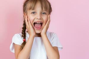 Beautiful little blonde girl with long hair in white T-shirt smiling on a pink background photo