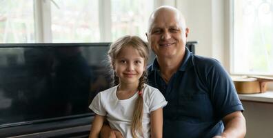 foto de gracioso dos personas antiguo abuelo pequeño interesado nieta sentado sofá narración bueno historia permanecer casa cuarentena la seguridad moderno diseño interior vivo habitación adentro