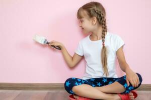 un azul ojos rubia niña en un blanco t camisa es sonriente y participación cepillo para renovación en el para niños habitación en contra el rosado antecedentes foto