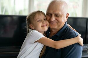 Senior grandfather with small granddaughter indoors sitting at table. photo