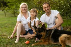 retrato de un extendido familia con su mascota perro sentado a el parque foto