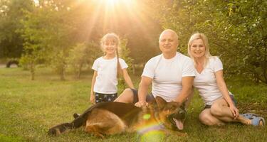 retrato de un extendido familia con su mascota perro sentado a el parque foto