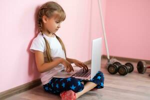 home, leisure, technology and internet concept - little student girl with laptop computer at home photo