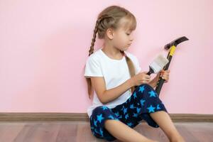 a blue eyed blonde girl in a white t shirt is smiling and holding brush for renovation in the children's room against the pink background photo