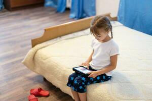 Portrait of cutie little girl playing on digital tablet while sitting at home in living room. photo