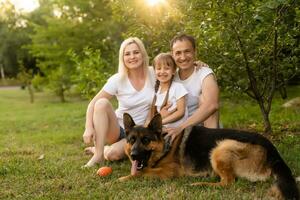 retrato de un extendido familia con su mascota perro sentado a el parque foto