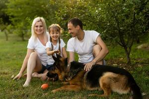 retrato de un extendido familia con su mascota perro sentado a el parque foto