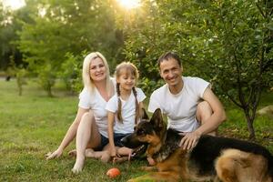 retrato de un extendido familia con su mascota perro sentado a el parque foto